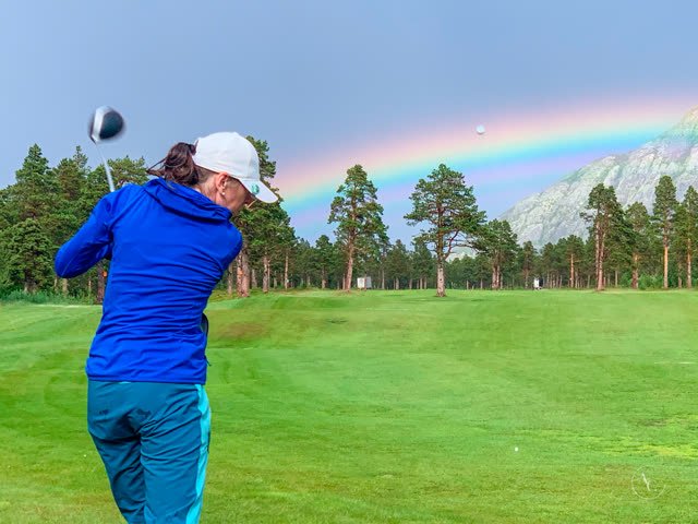 Golfspiller i utslaget med regnbue over furuskogen